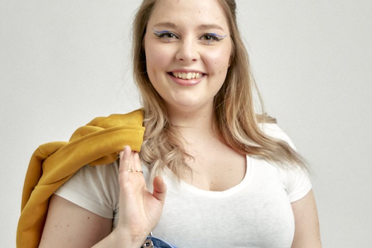 Johanna Gradl mit langen Haaren und Dutt, eine Jacke über der Schulter und auf einer Seite offenen Latzhose, lachend