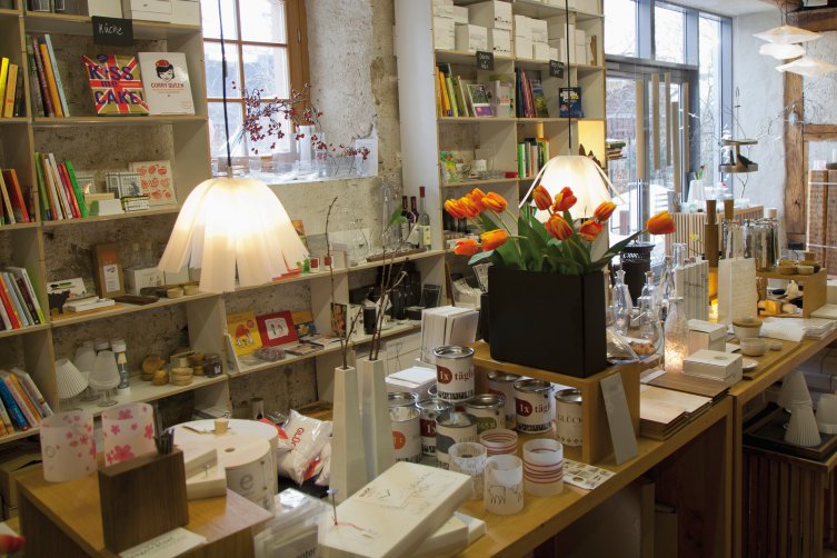 Ein Ausstellungstisch mit Deko-Artikeln, Konservendosen und weiteren Non-Book-Artikeln vor einem Bücherregal im Hintergrund.
